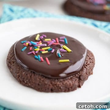 Close up of a keto brownie cookie on a white plate, over a colorful teal napkin, highlighting the glossy glaze and sprinkles.