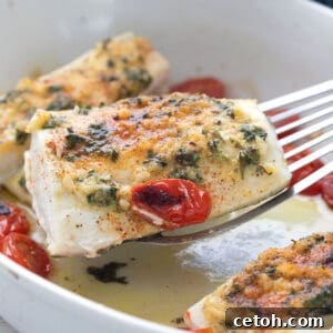 Zesty Lemon Garlic Baked Halibut 2 A fork lifting a piece of perfectly baked halibut with visible garlic and lemon, just removed from a white baking dish.