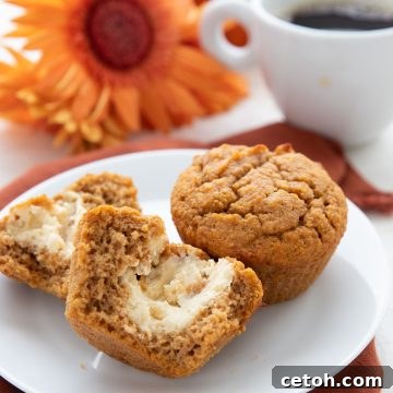 A keto pumpkin muffin broken open on a white plate to show the cream cheese center.