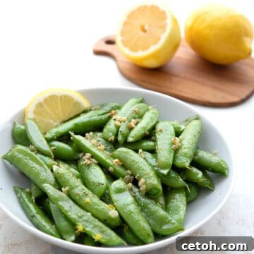 Sautéed sugar snap peas with lemon and garlic in a white serving dish.