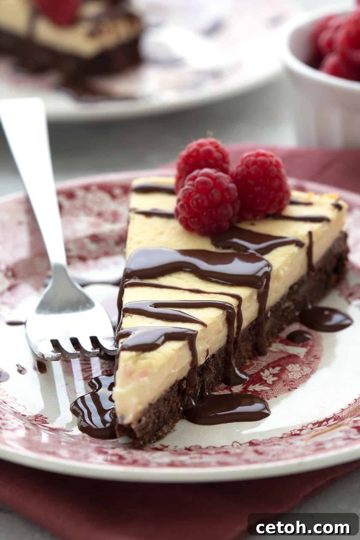 Close up shot of a slice of Keto Brownie Cheesecake on a red patterned plate, highlighting its rich layers.