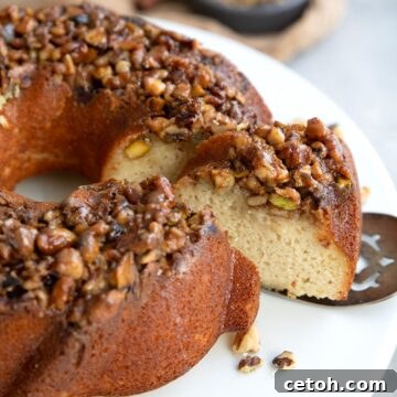 A slice of Baklava Bundt Cake being pulled away from the rest of the cake on a silver server.