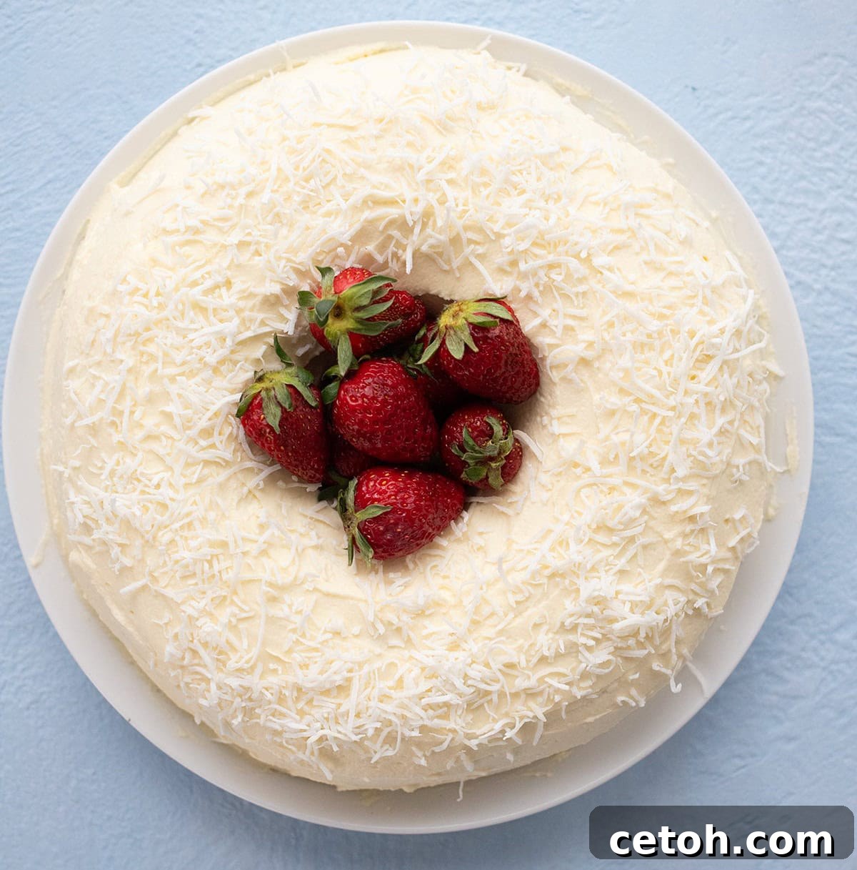 Top down image of a keto coconut bundt cake on a white plate with strawberries piled up in the center.