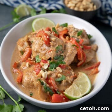 Slow Cooker Peanut Chicken in a white serving dish on a blue table with peanuts in the background.