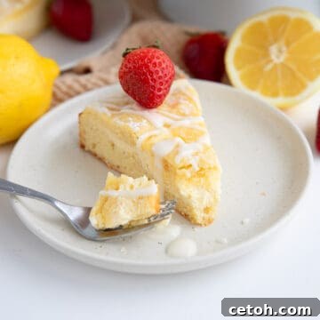 Close up shot of a slice of keto lemon coffee cake on a white plate, with a strawberry on top.