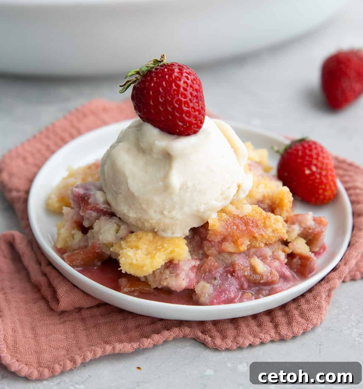 A serving of Strawberry Rhubarb Keto Dump Cake on a white plate with sugar free vanilla ice cream on top.