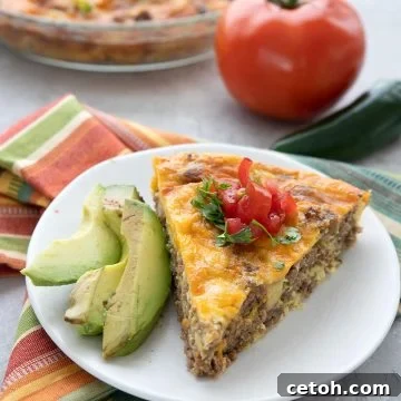 A slice of taco pie on a white plate with slices of avocado. A tomato and some jalapeno in the background.