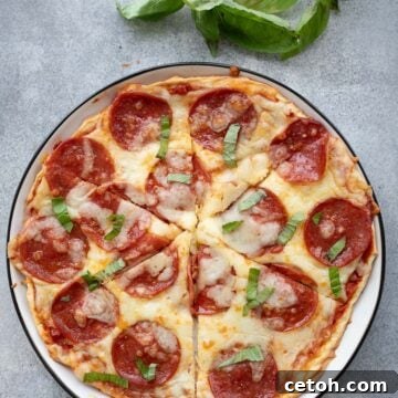 Top down image of cottage cheese protein pizza on a white plate with a sprig of fresh basil.