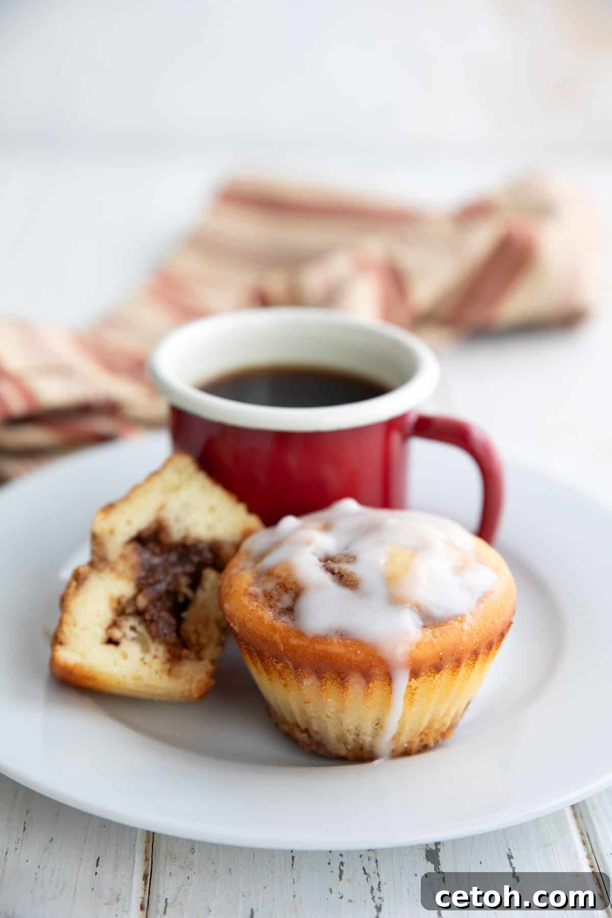Two Cinnamon Roll Protein Muffins with a cup of coffee on a white plate.