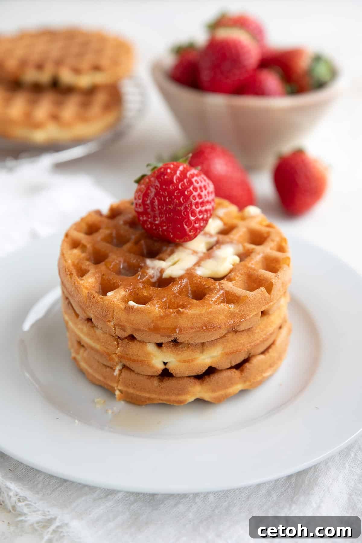 Three perfectly golden keto waffles stacked on a white plate, crowned with a fresh strawberry.