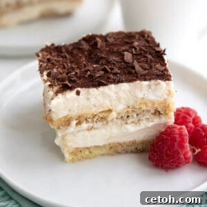 A slice of Keto Tiramisu on a white plate with raspberries.
