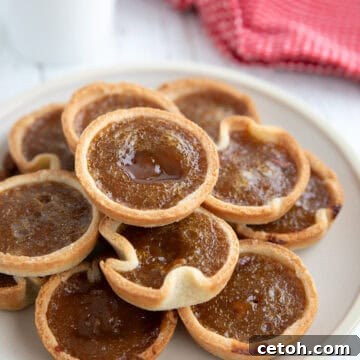 Decadent Keto Butter Tarts 5 A plate of delightful Keto Butter Tarts, glistening and perfectly baked, set against a pristine white wooden table.