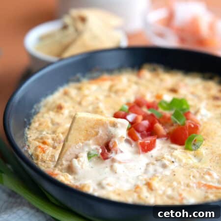 A keto cracker digging into a bowl of Baked Shrimp Dip.