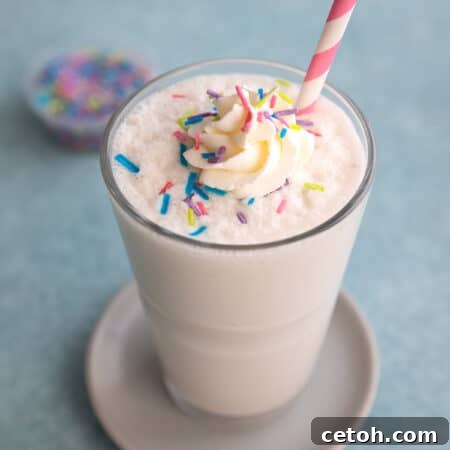 A glass filled with vanilla protein shake with whipped cream and sprinkles on top.