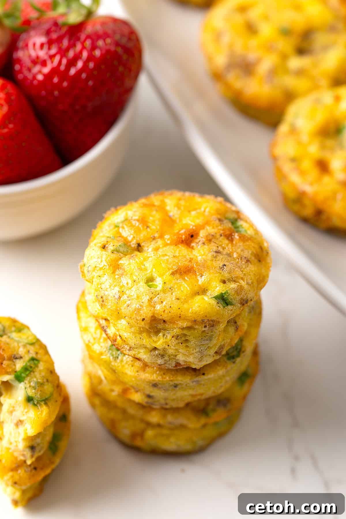 Effortless Keto Slow Cooker Breakfast Bake 2 A perfectly arranged stack of golden keto egg muffins on a sophisticated marble tabletop, with fresh, juicy strawberries artfully blurred in the background, creating an inviting morning scene.
