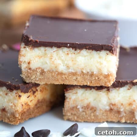 Close up shot of three chocolate coconut layer bars on a white plate with some chocolate chips.