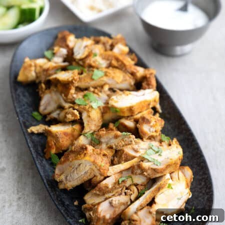 Effortless Loaf Pan Chicken Shawarma 2 Pieces of chicken shawarma piled up in a black oval platter on a gray concrete table.