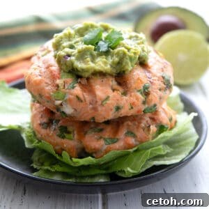 Two salmon burgers piled up on a black plate with guacamole on top, highlighting the finished dish.