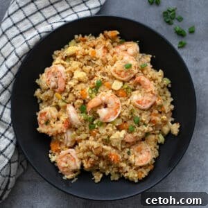 Top-down image of a black bowl filled with perfectly cooked fried cauliflower rice and plump shrimp, presented on a rustic gray surface.