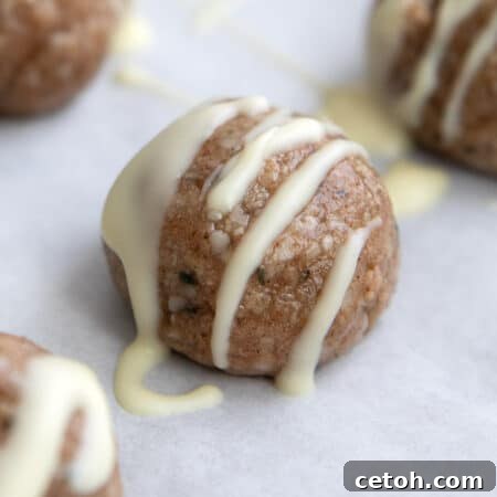Cinnamon Bun Protein Bites 2 Close up shot of a Cinnamon Roll Protein Bite with white chocolate drizzle on white parchment paper.