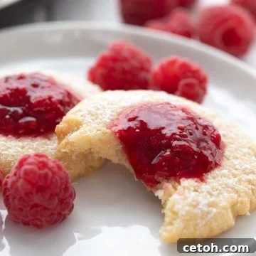 Close up shot of a keto jam thumbprint cookie on a white plate with raspberries in the background.