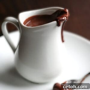 A small white pitcher filled with rich, glossy keto chocolate sauce, ready to be poured and enjoyed.