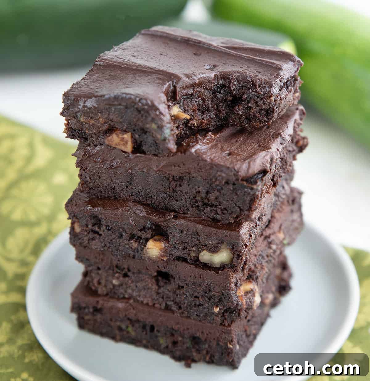 An enticing stack of rich keto zucchini brownies, with a corner gently missing from the top one, inviting you to take a bite and experience its moist texture.