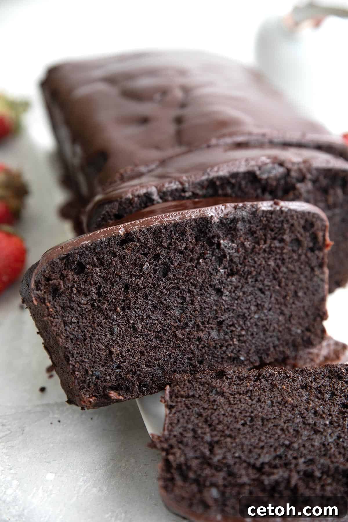 A tempting slice of sugar-free keto chocolate pound cake, artfully leaning against the remainder of the cake, beautifully showcasing its perfect crumb and glistening glaze.