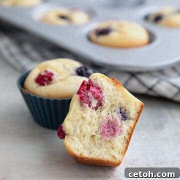 A Keto Pancake Muffin broken open to show the inside, in front of a pan full of muffins.