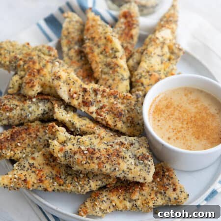 Keto chicken tenders with everything bagel seasoning piled up on a white plate over a blue and white striped napkin.