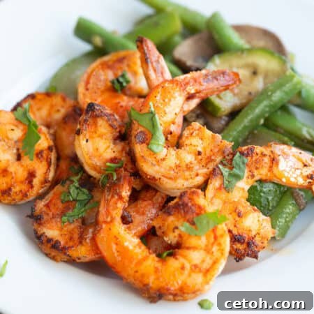 Chili Garlic Shrimp on a white plate with sautéed vegetables, with chopped parsley on top.