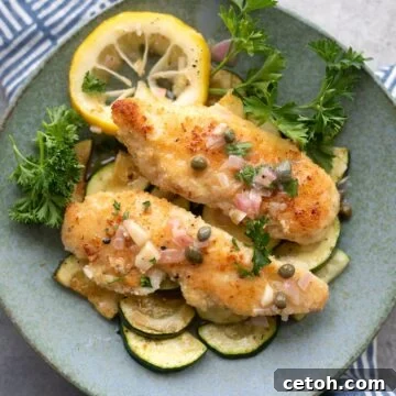 Top down image of Keto Chicken Piccata over sautéed zucchini, with slices of lemon and sprigs of parsley.