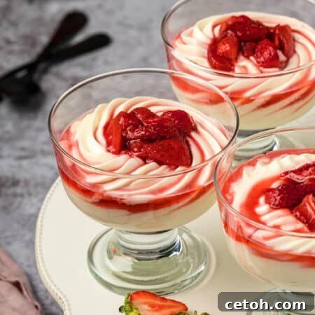 Three elegant dessert glasses brimming with fluffy mascarpone mousse, garnished with vibrant roasted strawberries, presented on a pristine white cake stand.