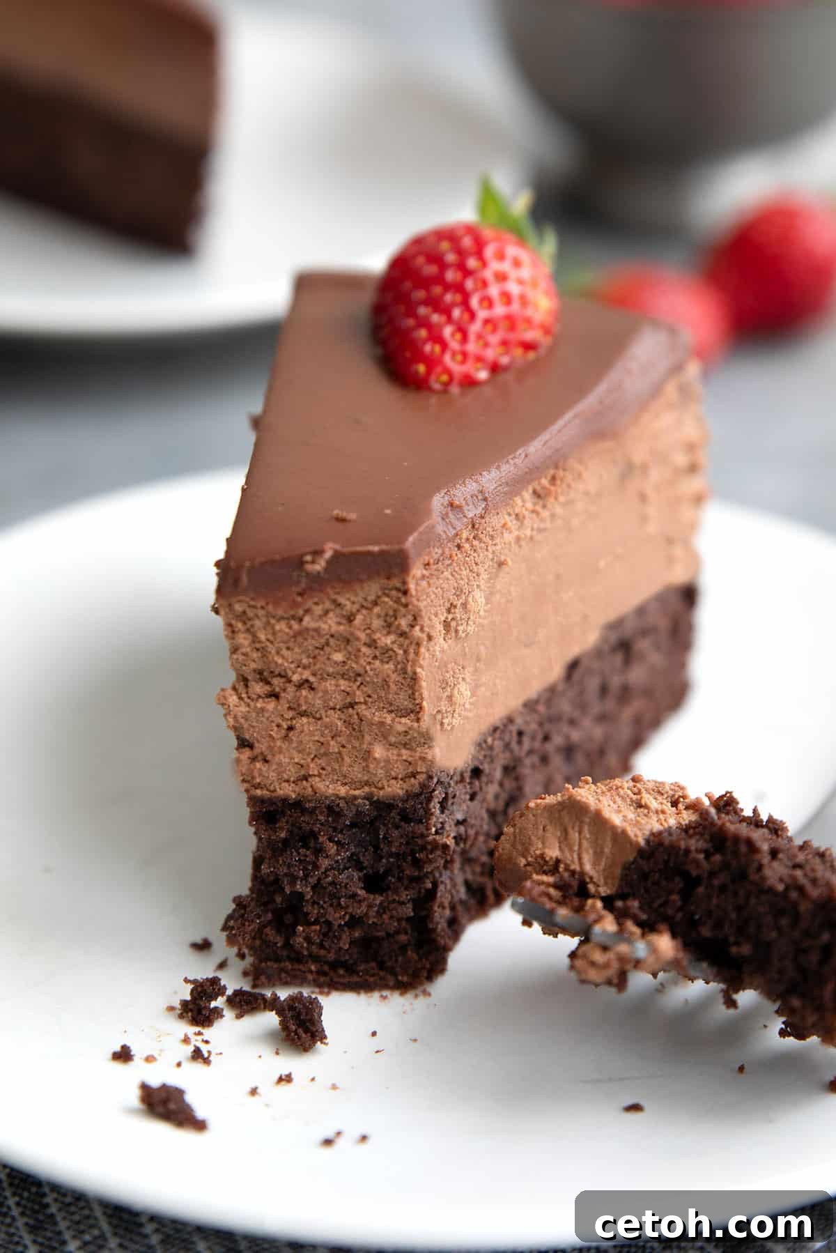 Close up shot of a slice of Keto Chocolate Mousse Cake on a white plate, with a forkful taken out of it.