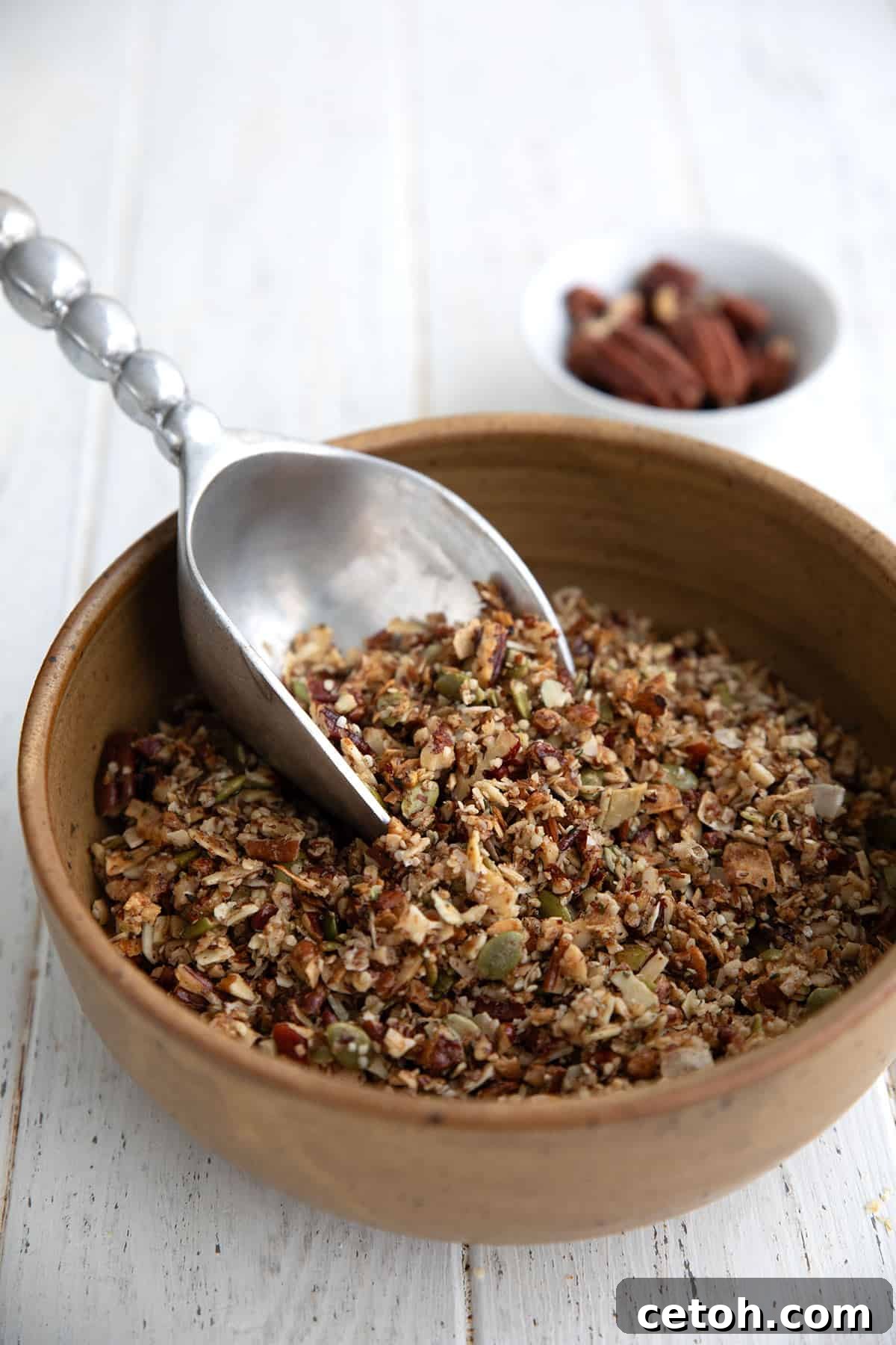 Low-Carb Keto Granola Recipe for Air Fryer (Crunchy & Fast) 2 Keto Air Fryer Granola in a large brown ceramic bowl with a metal scoop digging into it.