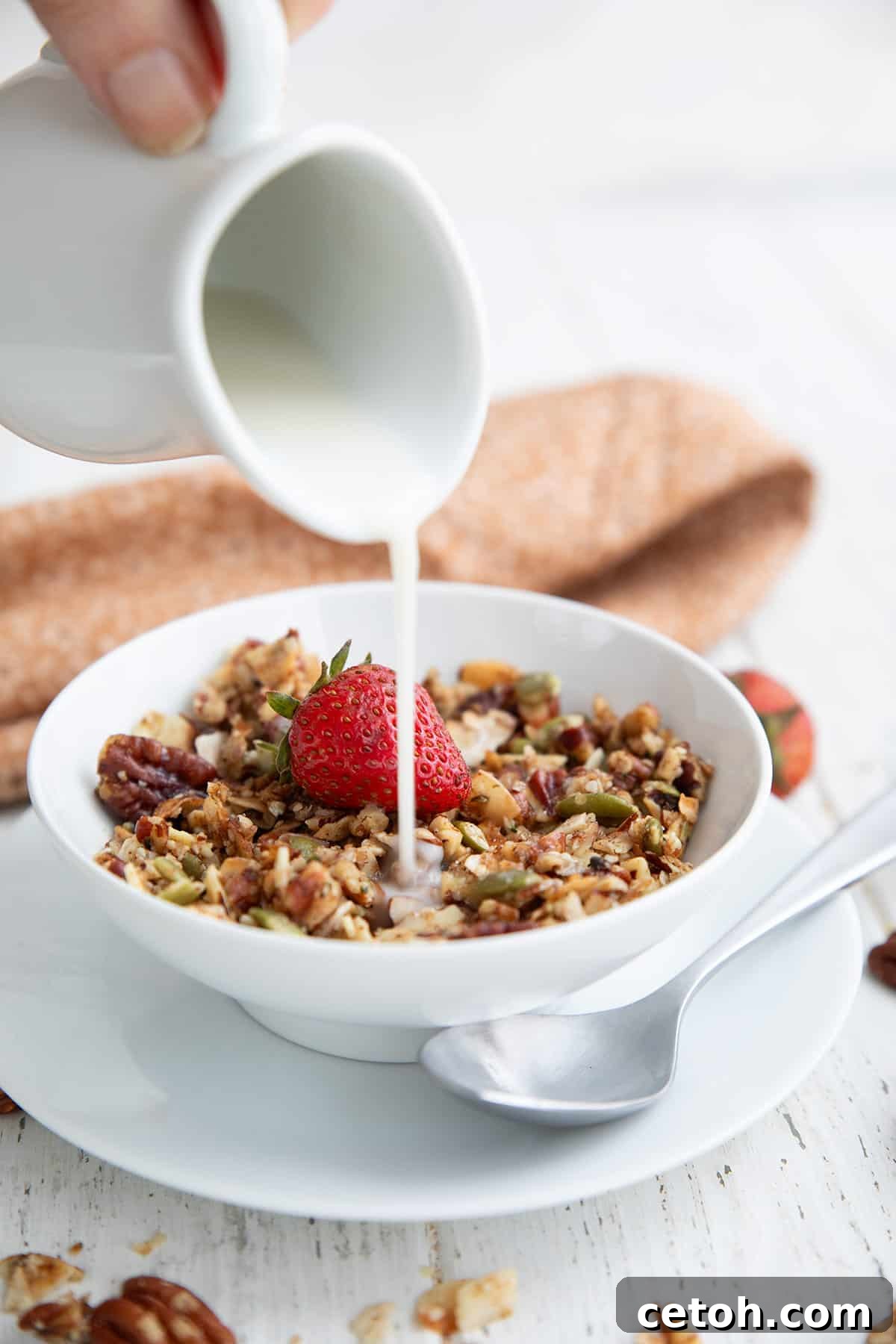 Low-Carb Keto Granola Recipe for Air Fryer (Crunchy & Fast) 6 Almond milk being poured from a small white pitcher onto Keto Air Fryer Granola in a white bowl.