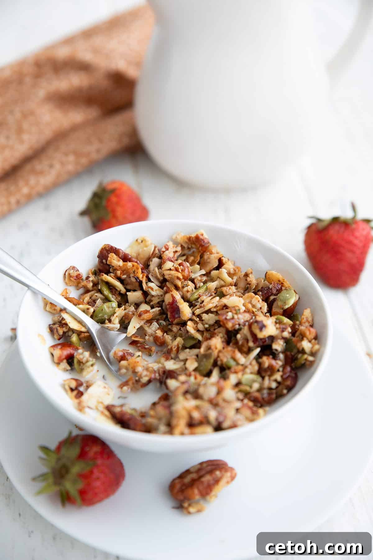 Low-Carb Keto Granola Recipe for Air Fryer (Crunchy & Fast) 8 A spoon digging into a small white bowl filled with Keto Air Fryer Granola, with strawberries arranged around it.