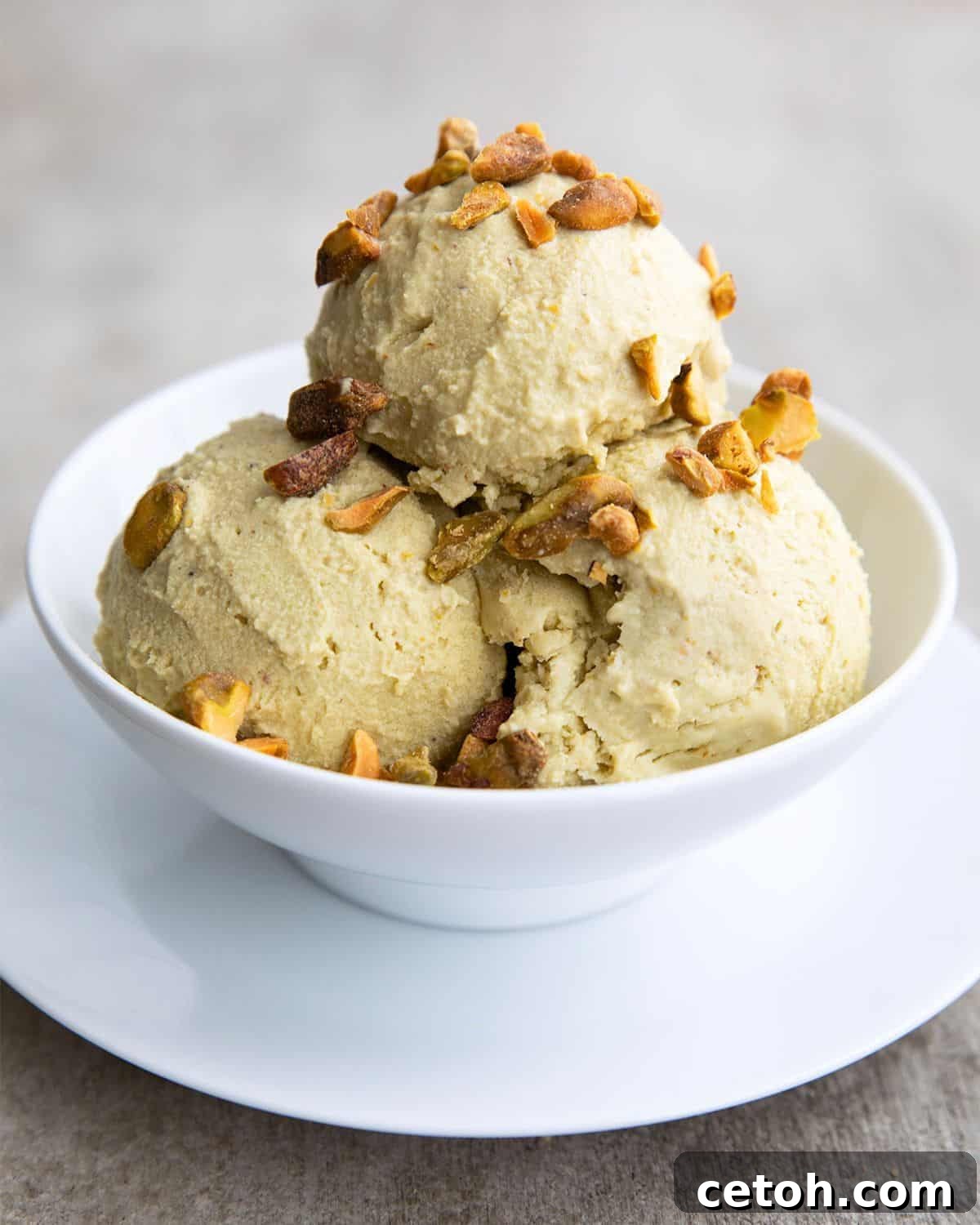 A white bowl with three scoops of keto pistachio ice cream, topped with chopped, salted pistachios.