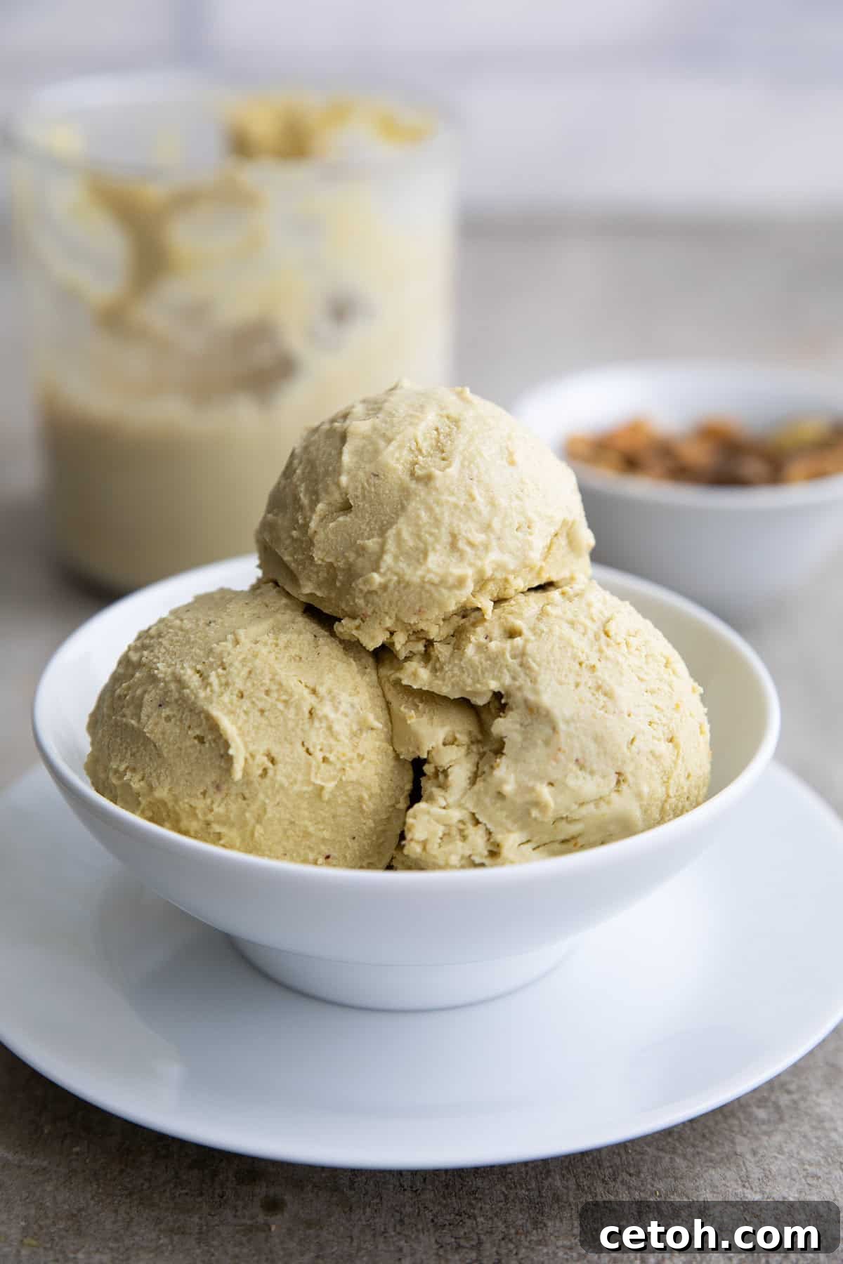 A white bowl with three scoops of keto pistachio ice cream, with a bowl of pistachios and the ice cream container in the background.