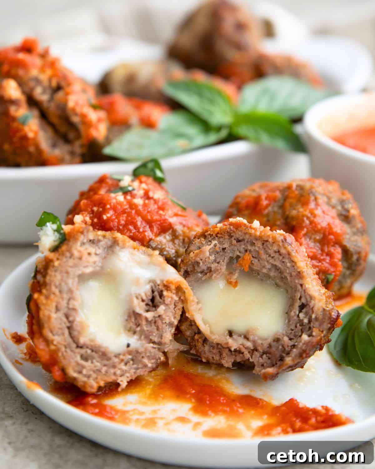 Three air fryer stuffed meatballs covered with tomato sauce on a white plate. One of the meatballs is cut in half to show the cheese inside.