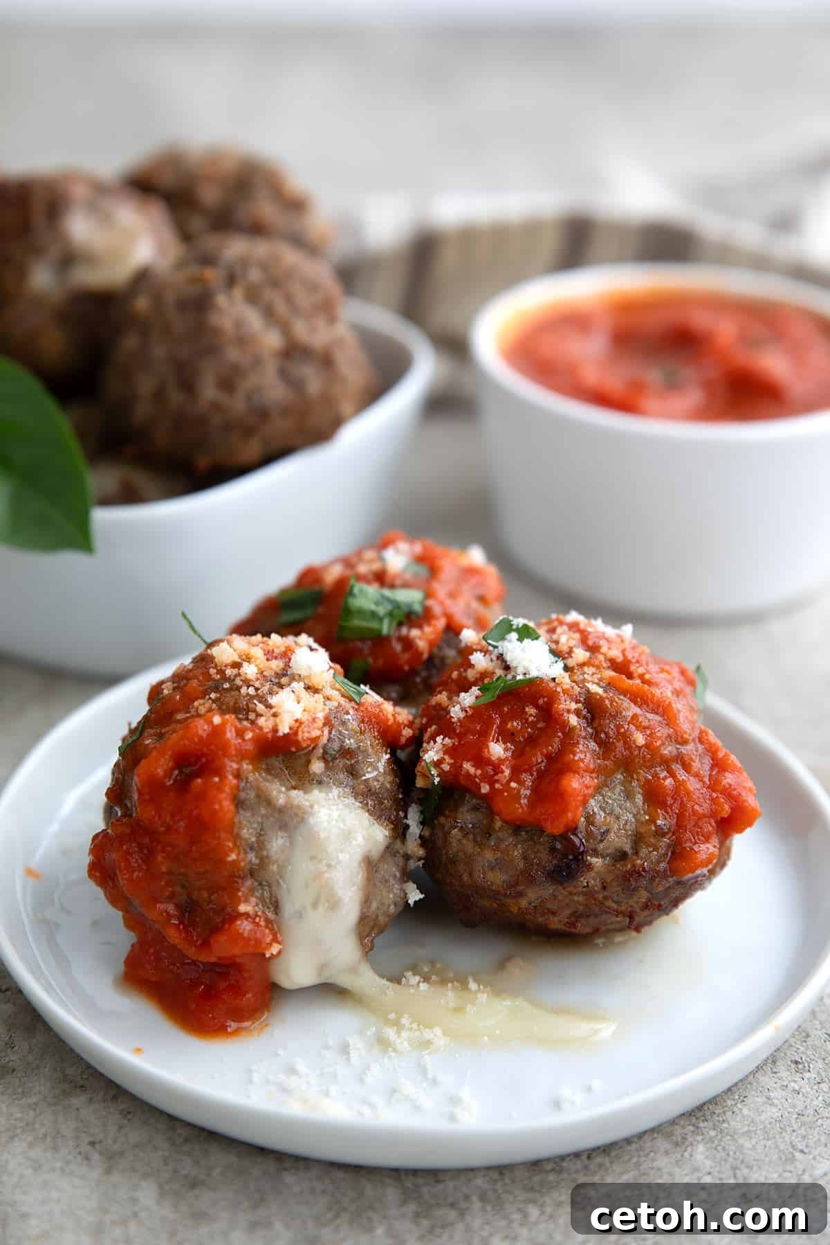 Three keto stuffed meatballs topped with tomato sauce, parmesan, and chopped basil on a white plate.