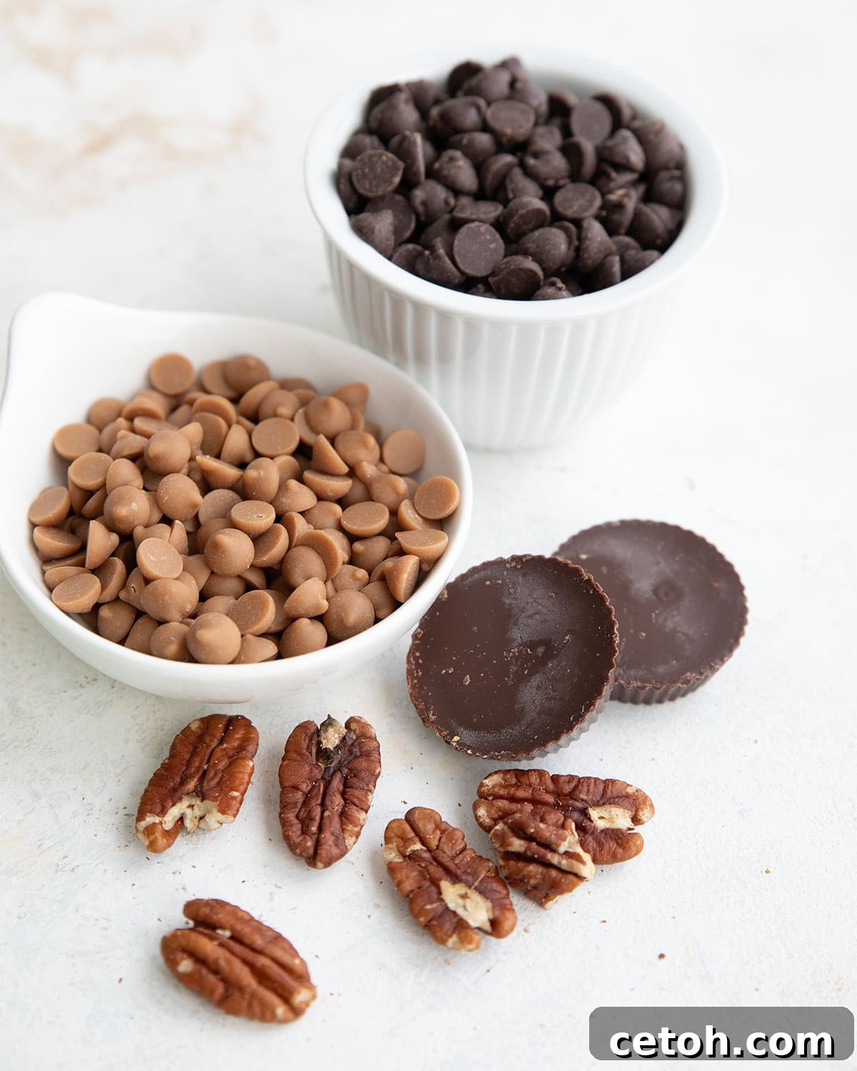Chocolate Chip Keto Cookie Bars Loaded with Nuts 4 Keto chocolate chips and peanut butter chips in white bowls, with two peanut butter cups and some pecans in front.