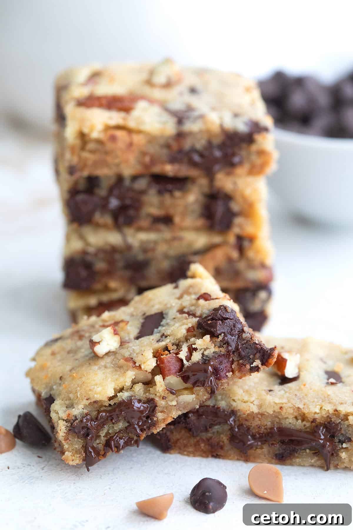 Chocolate Chip Keto Cookie Bars Loaded with Nuts 8 Two keto cookie bars leaned against each other on a white table top, with a stack of more bars in behind.