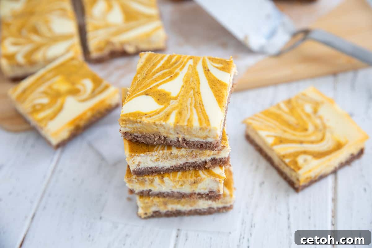 Keto Pumpkin Swirl Cheesecake Bars 7 A stack of keto pumpkin swirl cheesecake bars on a white wooden table.